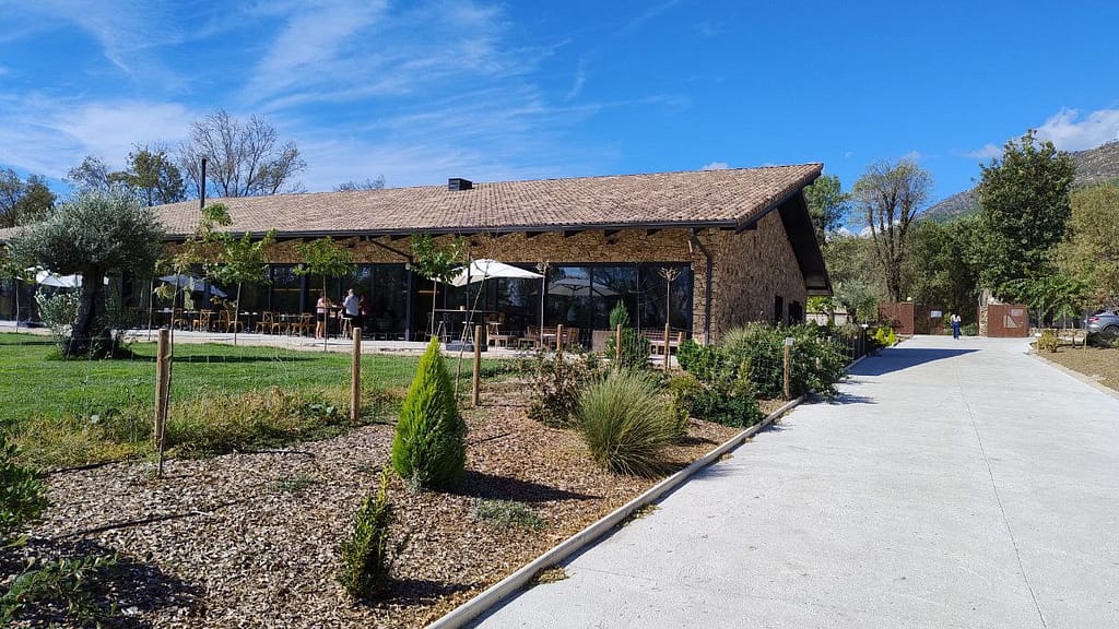 Fachada rústica de piedra de Huellas del Tietar con ventanales modernos, jardín de olivos y Sierra de Gredos de fondo en Lanzahita