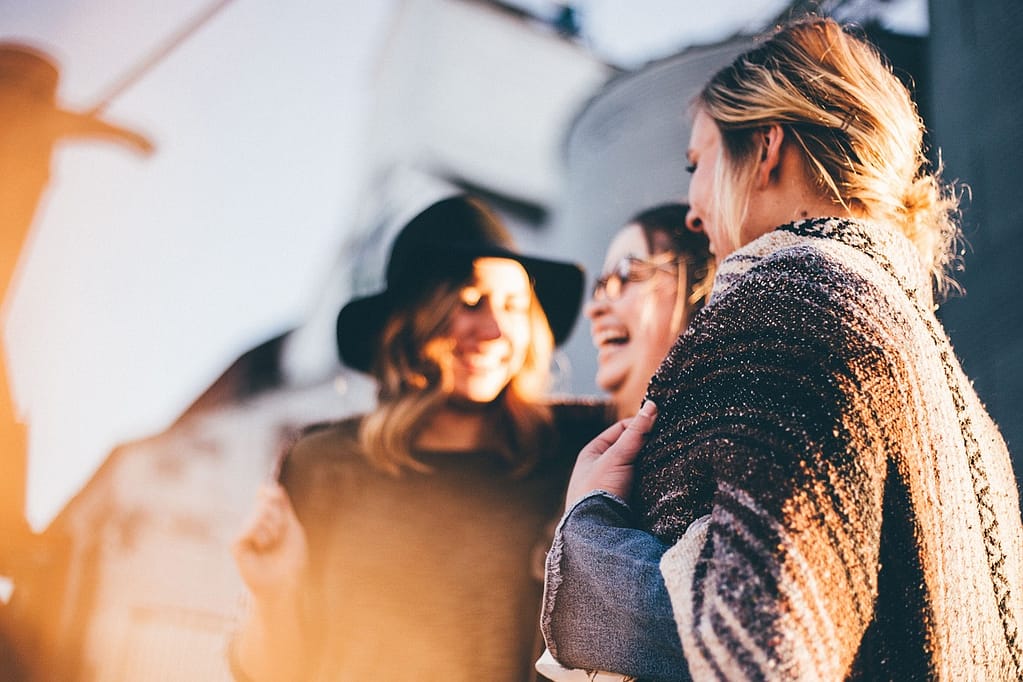 Tres amigas sonriendo y charlando en la calle, reflejando amistad y un momento de conexión.