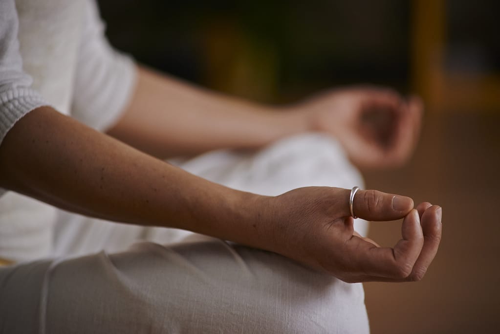 Primer plano de manos apoyadas en las rodillas con las palmas hacia arriba y dedos juntos (mudra), en postura de loto para meditación profunda.