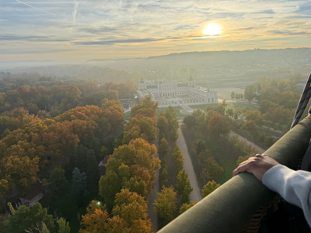 Vista aérea del Palacio Real de Aranjuez y sus jardines desde un globo, capturando el paisaje al amanecer.