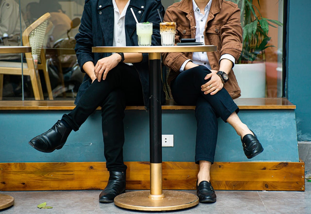 Dos personas sentadas juntas en una cafetería, torsos y piernas visibles, con un granizado de limón y un café sobre la mesa.