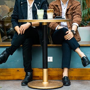 Dos personas sentadas juntas en una cafetería, torsos y piernas visibles, con un granizado de limón y un café sobre la mesa.