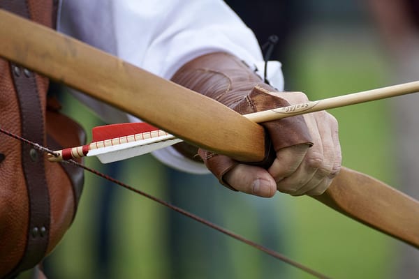 Mano con protector de cuero sosteniendo un arco tradicional de madera con flecha